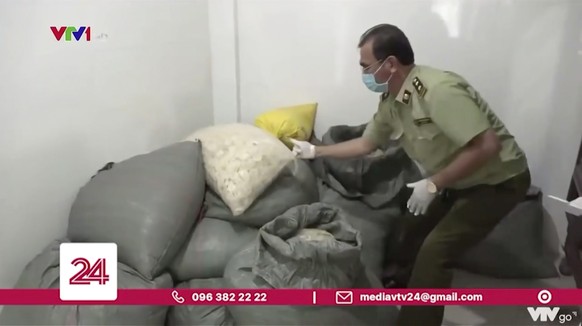 In this image from a video report by VTV, a police official grabs a sack of allegedly used condoms that are being packed for sale in Binh Duong province, Vietnam on Sept. 10, 2020. Vietnamese police s ...