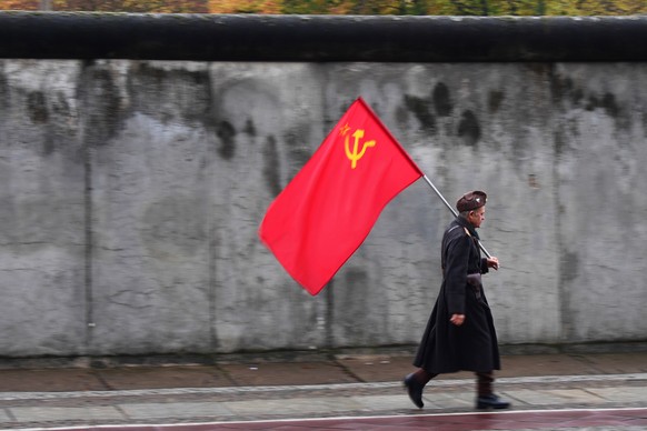epaselect epa07983519 A man in a uniform with a soviet flag, protesting against dictatorship of capitalism, walks past the wall after the end of the official celebrations of the 30th anniversary of th ...