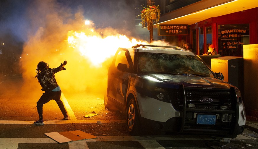 epaselect epa08457147 A man tries to light his cigarette from the flames of a burning Boston Police cruiser during calshes with police amid demonstrations over the death of George Floyd, who died in p ...