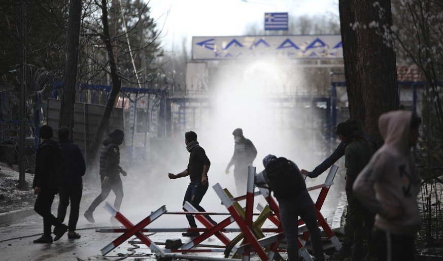 In this photo taken Wednesday, March 11, 2020, Greek security force use teargas against stone-throwing migrants at the Turkish-Greek border in Pazarkule, Edirne region, Turkey. Thousands of migrants m ...