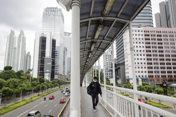 epaselect epa08919714 A man wearing a protective face mask walks on a pedestrian bridge at a business area in Jakarta, Indonesia, 05 January 2021. The country&#039;s inflation rate through 2020 record ...