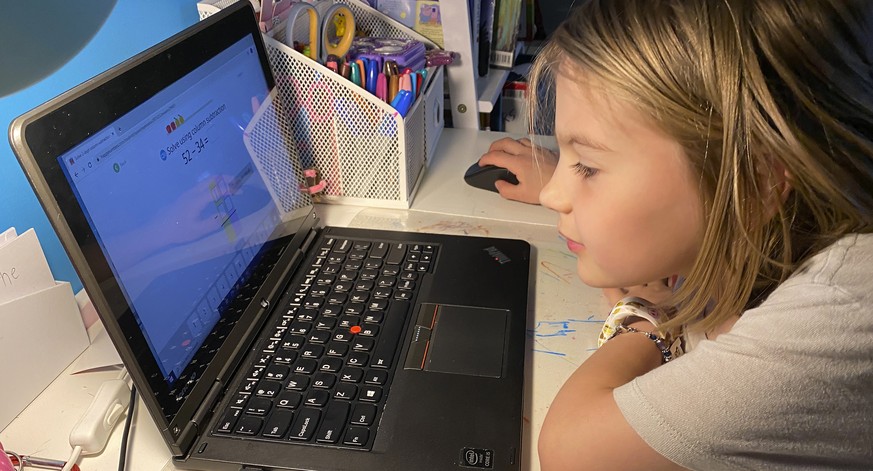 This April 9, 2020, photo released by Kara Illig shows her daughter, Ainslie Illig, 8, on her computer in Ebensburg, Pa. The frustration of parents is mounting as more families across the U.S. enter t ...