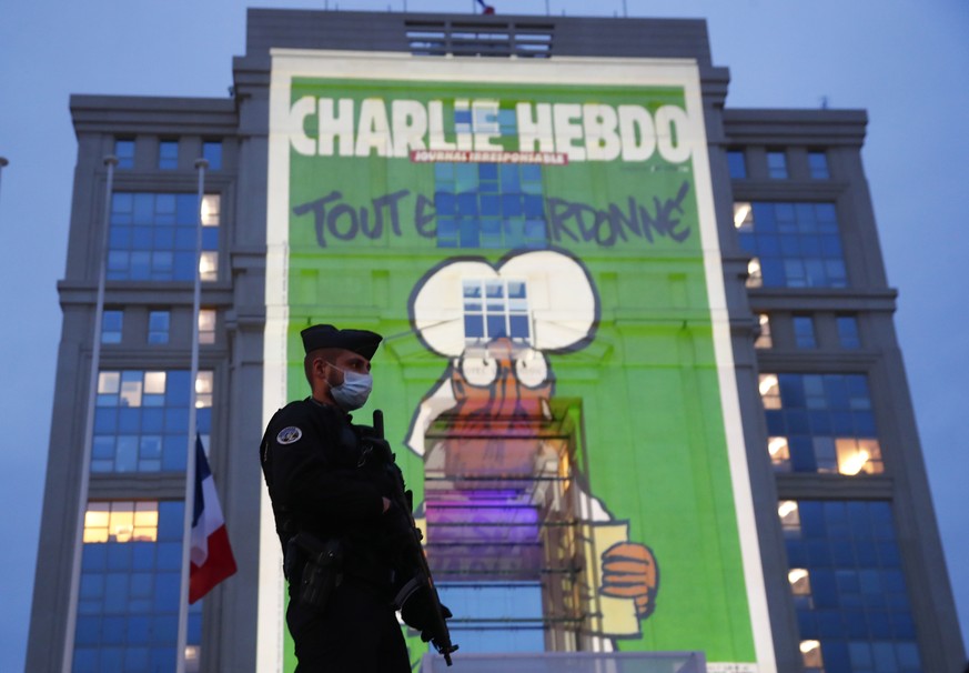 epa08762560 A police officer stands by as cartoons from French satirical newspaper Charlie Hebdo are projected onto buildings in central Montpellier in France, 21 October 2020. The cartoons of Prophet ...