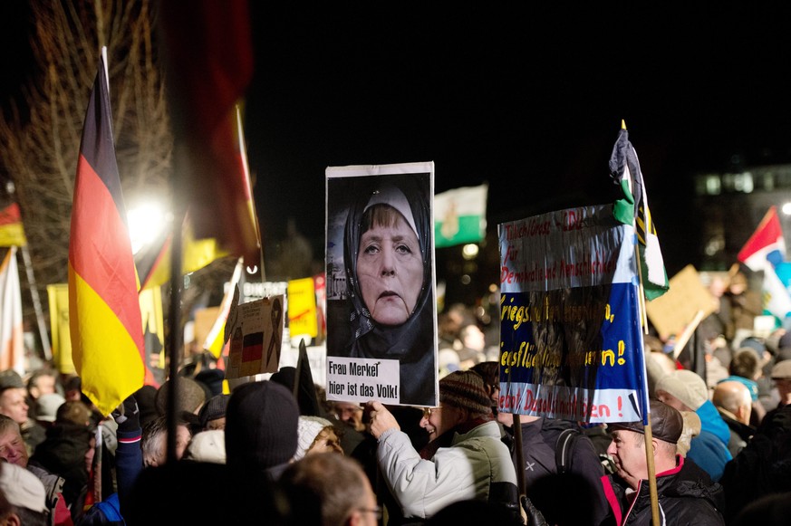 epa04557360 Participants in a rally with the Anti-Islamic Pegida (Patriotic Europeans against the Islamization of the West) movement hold up a picture of Chancellor Merkel wearing a headscarf written  ...