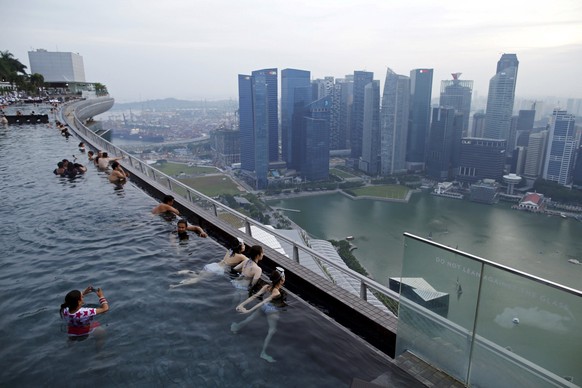 Tourists look at the skyline of the city from an infinity pool atop the 57 storey high Marina Bay Sands hotel in Singapore, in this July 10, 2015 file photo. Singapore-based wealth managers, already u ...