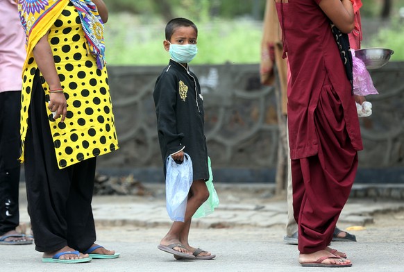 epa08373219 A boy wearing a face mask waits for his turn to receive free food from the authorities near one of the hot spot where coronavirus cases continue to rise in Noida Gautam Buddh Nagar outskir ...