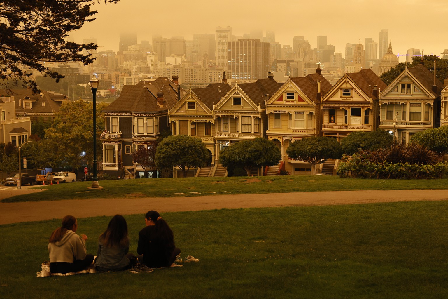 epaselect epa08657767 People sit at Alamo Square under an orange and yellow overcast sky overlooking the The Painted Ladies, the iconic row of historical Victorian homes with a downtown backdrop, in t ...