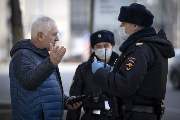 Russian police officers, wearing face masks to protect from coronavirus, check documents of a man to ensure a self-isolation regime due to coronavirus, in Moscow, Russia, Monday, April 13, 2020.Presid ...