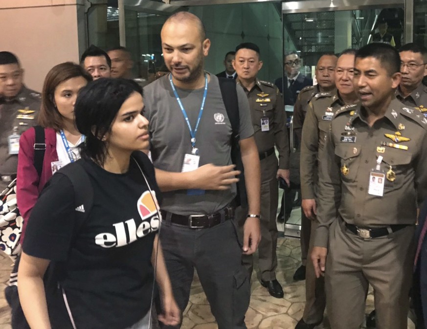 In this photo released by the Immigration Bureau, Saudi woman Rahaf Mohammed Alqunun, foreground walks by Chief of Immigration Police Maj. Gen. Surachate Hakparn, right, before leaving the Suvarnabhum ...