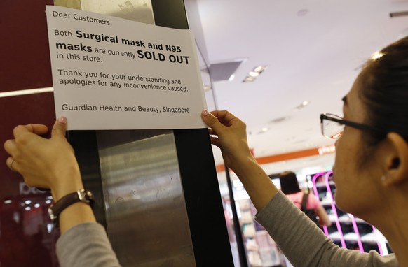 epa08171742 A staff member puts up signs showing protective masks have been sold out at a pharmacy in Singapore, 28 January 2020. Residents in Singapore stocked up on protective masks, causing many sh ...