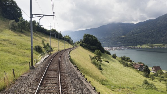 Railway tracks and Lake Zug to the right between Walchwil, canton of Zug, and Goldau, canton of Schwyz, pictured amidst a green hilly landscape from a train travelling from Zurich to Bellinzona, in th ...