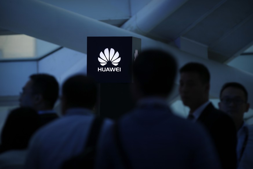 In this May 26, 2016, photo, attendees stand near a pillar with the Huawei logo during a launch event for the Huawei Matebook in Beijing. As trade disputes simmer, Chinese telecommunications giant Hua ...