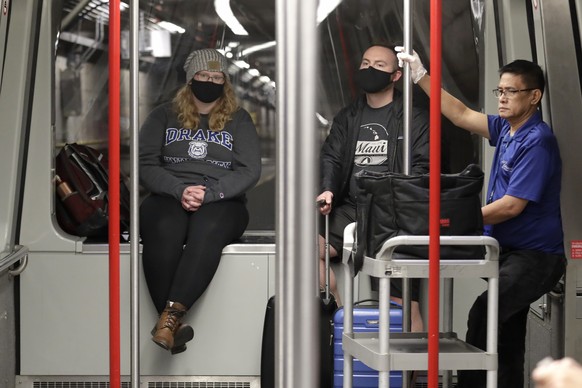 FILE - In this March 2, 2020 file photo, travelers Meredith Ponder, left, and Coleby Hanisch, both of Des Moines, Iowa, wear masks to remind them not to touch their faces as they ride a train at Seatt ...