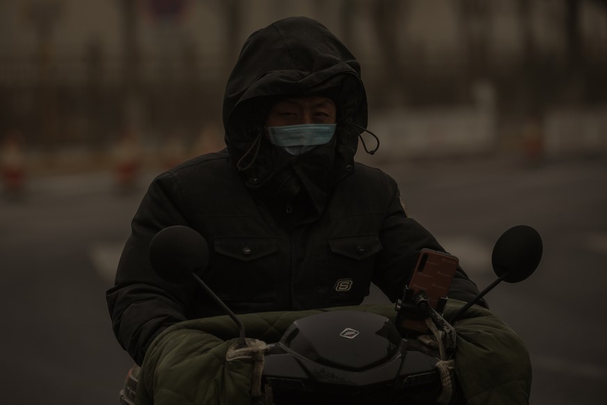 epa09075506 A man wearing a mask rides scooter in the street as the area is hit by sandstorm, in Beijing, China, 15 March 2021. According to the National Meteorological Center, floating sand and dust  ...