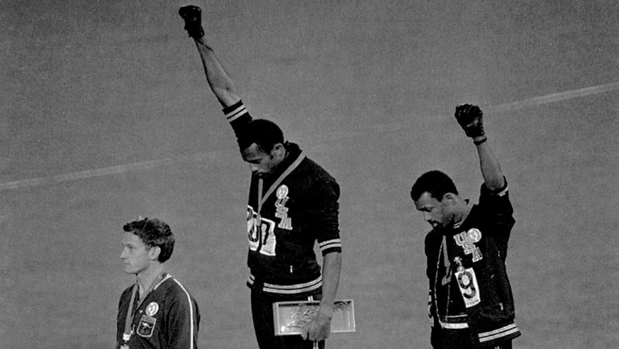 Extending gloved hands skyward in racial protest, U.S. athletes Tommie Smith, center, and John Carlos, stare downward October16, 1968 during the playing of the Star Spangled Banner after Smith receive ...