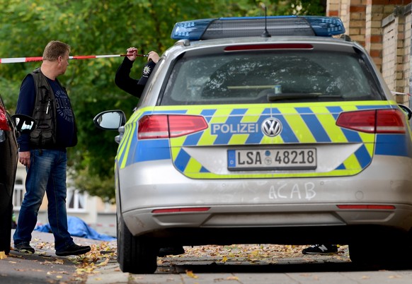 epa07907486 A police officer passes the covered corpse of a dead person at a Synagogue after a shooting in Halle, Germany, 09 October 2019. According to the police two people were killed in shootings  ...