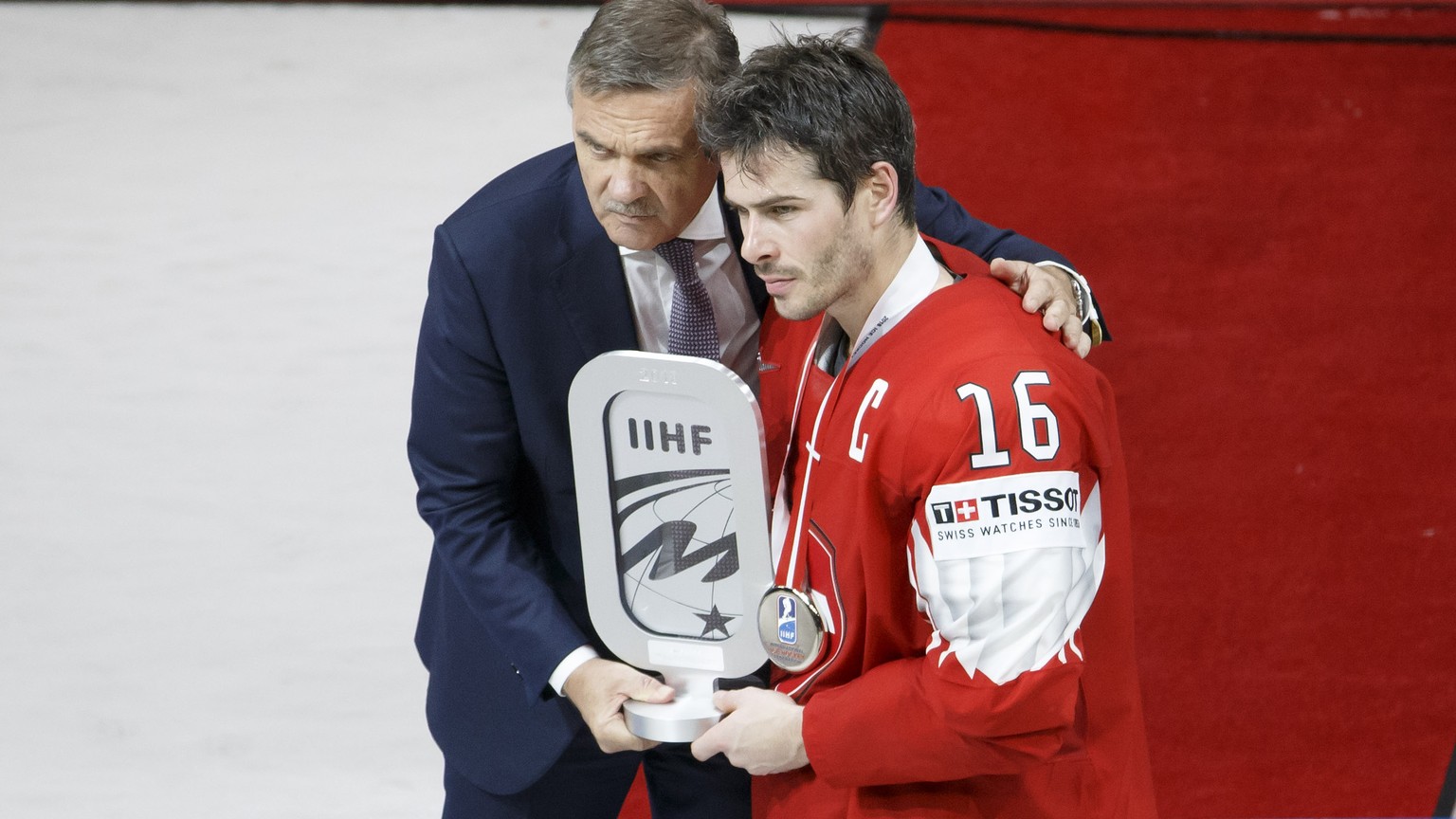 Rene Fasel, left, President of IIHF, gives the silver trophy to Switzerland&#039;s defender Raphael Diaz, right, after team Switzerland losing agains team Sweden, during the shootout of the IIHF 2018  ...