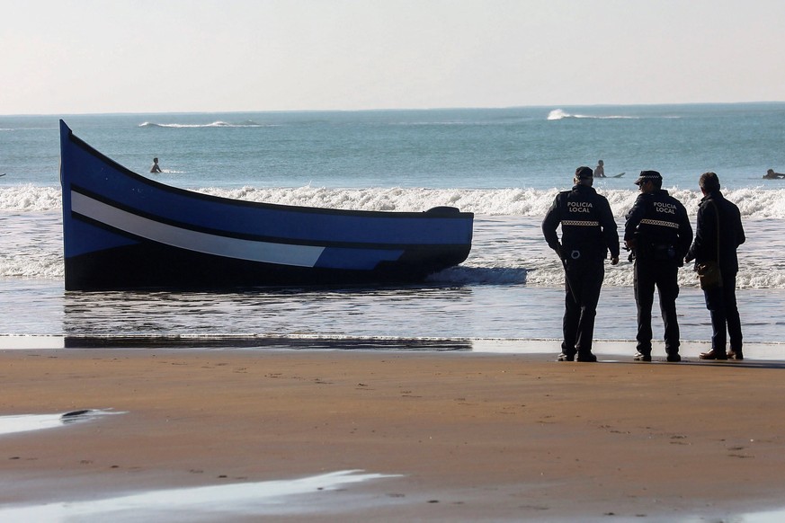 epa07219123 Local policemen stand guard next to a boat in which a total of 30 migrants managed to reach Santa Maria del Mar beach in Cadiz, southern Spain, 09 December 2018. Spanish authorities report ...