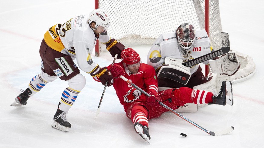 Lausanne&#039;s forward Brian Gibbons, of U.S.A., center, vies for the puck with Geneve-Servette&#039;s defender Mike Voellmin, left, and goaltender Gauthier Descloux, right, during a National League  ...