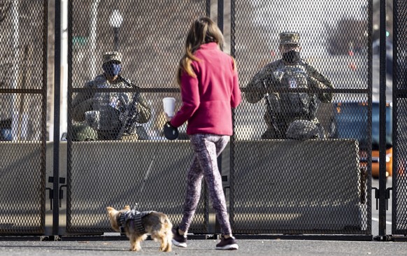epa08942308 National Guard troops stand guard as a woman walks her dog past at the fence line around the US Capitol building in Washington, DC, USA, 16 January 2021. At least twenty thousand troops of ...