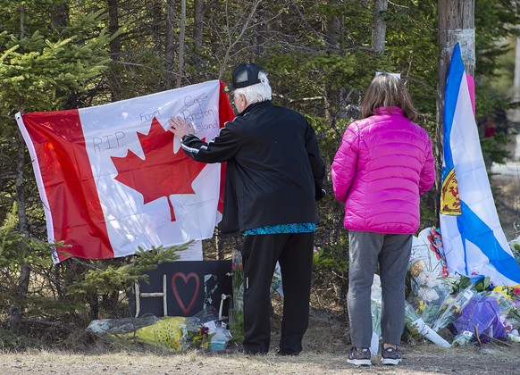 In this Wednesday, April 22, 2020, photo, a couple place a flag at a memorial in Portapique, Nova Scotia, following Saturday&#039;s shooting rampage. (Andrew Vaughan/The Canadian Press via AP)