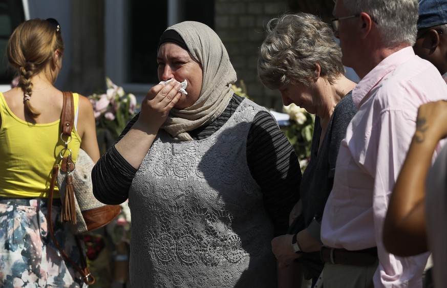 A woman puts her hand to her face as she respects a minute&#039;s silence near to Grenfell Tower in west London Monday, June 19, 2017. Tens of people died when a fire engulfed an high-rise apartment b ...