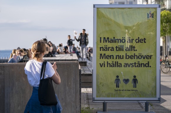 People enjoy the warm evening weather in Malmo, Sweden, Tuesday May 26, 2020 as a sign reads &#039;In Malmo everything is near. But now we need to keep a distance&#039;. Sweden has defended its respon ...