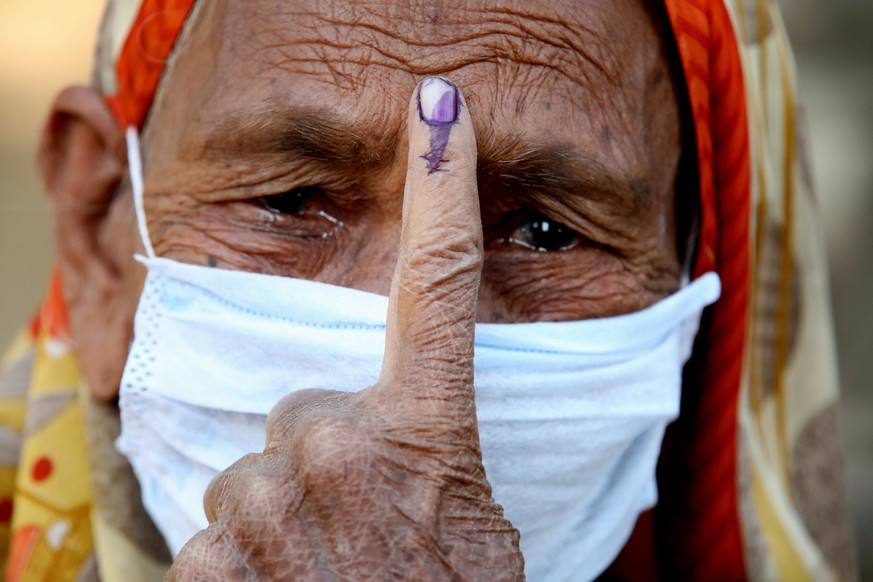 epa08794852 An Indian woman wearing a face mask shows her ink marked finger after casting her vote at a polling station during by-elections in Sanchi, about 60km from Bhopal, Madhya Pradesh, India, 03 ...