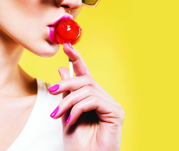 attractive woman eating red lollipop in sunglasses on yellow background