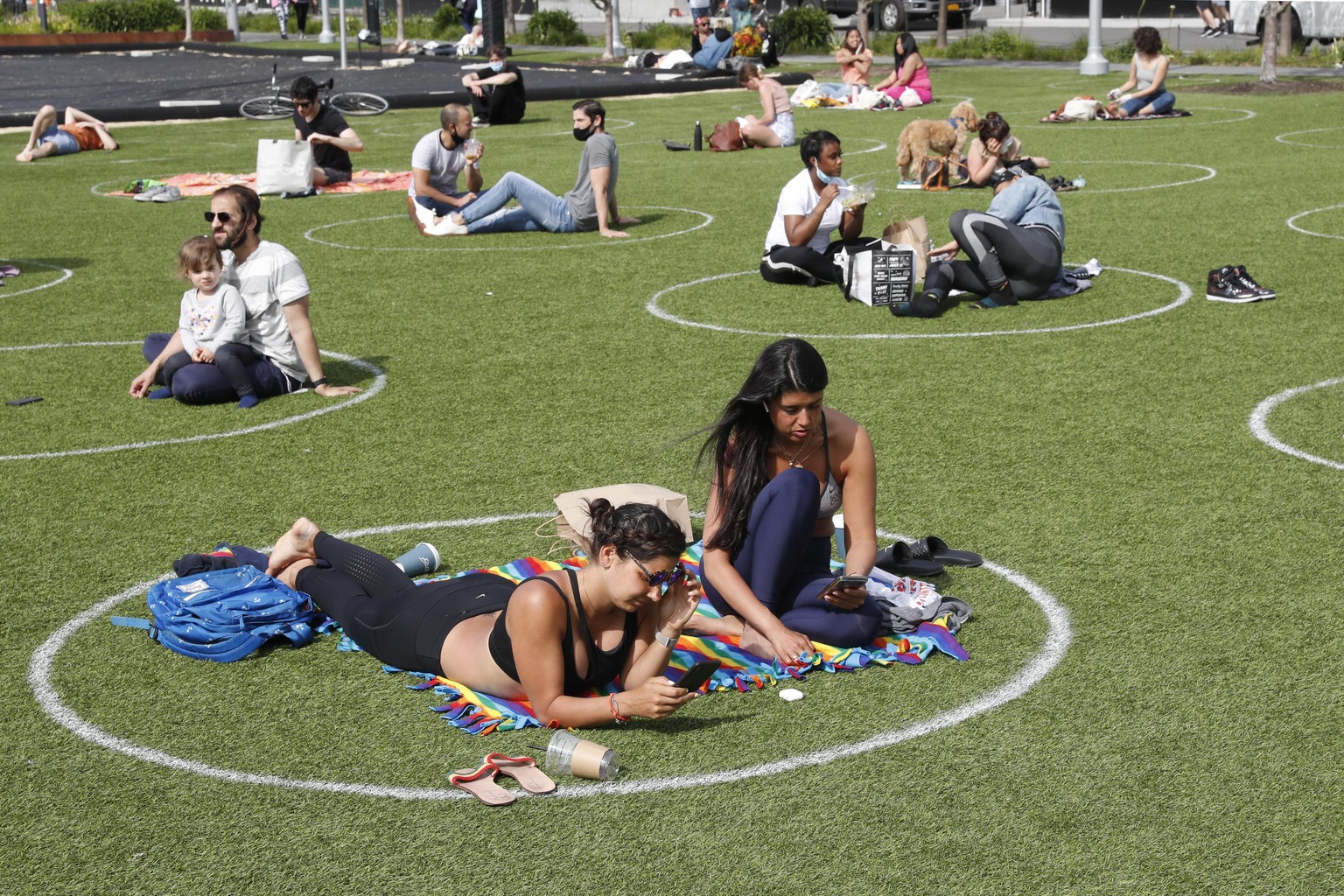 Two young women relax in a circle marked on the grass for proper social distancing in Brooklyn&#039;s Domino Park as others do the same to prevent the spread of coronavirus, Monday, May 18, 2020, in N ...