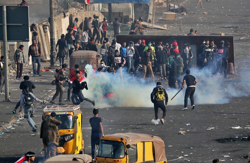 Anti-government protesters take cover while security forces use tear gas during clashes in central Baghdad, Iraq, Monday, Jan. 20, 2020. Iraqi security forces fired tear gas and live rounds during cla ...