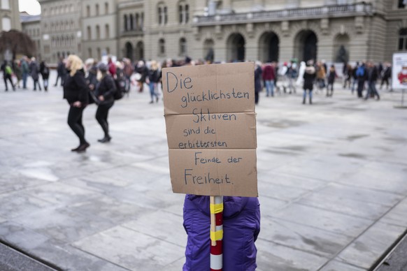 Ein improvisiertes Transparent formuliert einen diffusen Protest, waehrend eine Schar unmaskierter Leute zusammen ueber den Bundesplatz spaziert, am Sonntag, 13. Dezember 2020 in Bern. (KEYSTONE/Aless ...