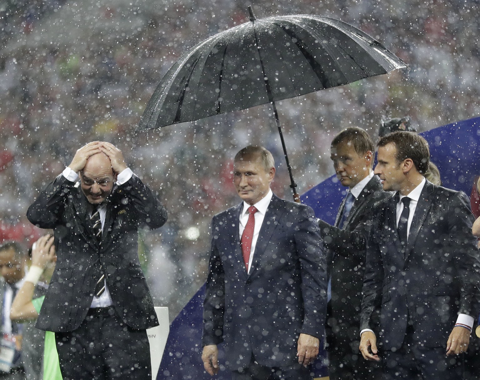 FIFA President Gianni Infantino, left, gestures as Russian President Vladimir Putin stands underneath an umbrella watched by French President Emmanuel Macron after the final match between France and C ...