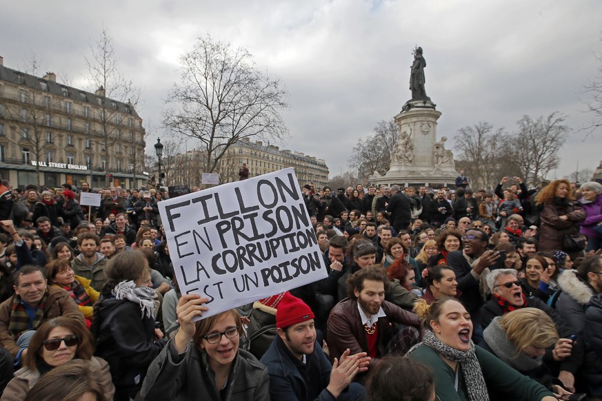 A man holds a placard reading &quot;Fillon Go To Jail, Corruption is a Poison&quot; as activists from left-wing parties and other groups attend a demonstration at the Place de la Republique against co ...