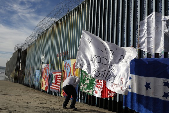 Joseph, an migrant from Honduras, plants a white flag with the words, &quot;peace and God with us,&quot; in front of the border wall during an art display on the border wall, topped with razor wire, T ...