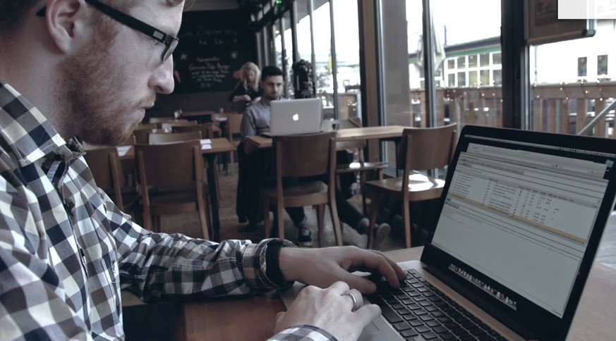 watson-Redaktor und Apple-User&nbsp;Can Külahcigil (im Hintergrund) in einem Café in Zürich: Wir haben Hacker Stefan Friedli (im Vordergrund) auf ihn angesetzt.&nbsp;Unser Arbeitskollege weiss, dass w ...