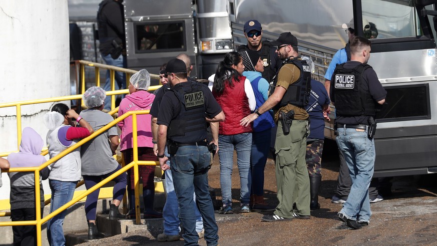 Handcuffed female workers are escorted into a bus for transportation to a processing center following a raid by U.S. immigration officials at a Koch Foods Inc., plant in Morton, Miss., Wednesday, Aug. ...