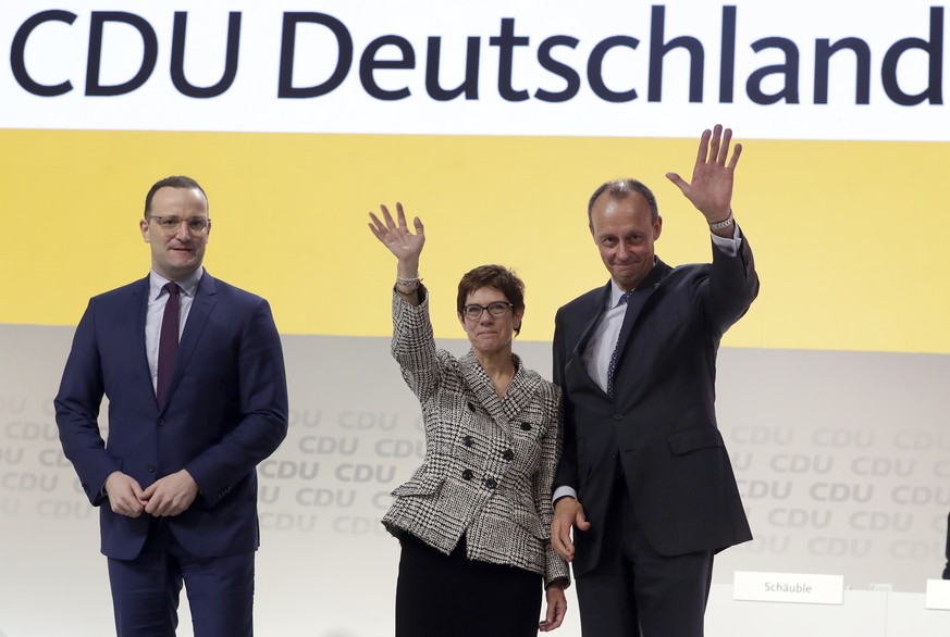 In this Friday, Dec. 7, 2018 photo then newly elected CDU chairwoman Annegret Kramp-Karrenbauer, center, is flanked by the defeated candidates Jens Spahn, left, and Friedrich Merz, right, as she waves ...