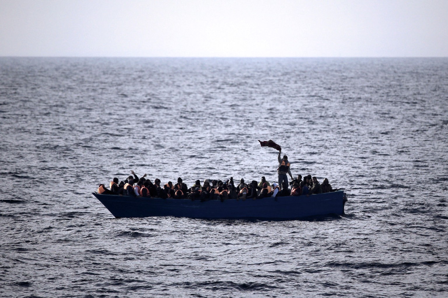 Migrants and refugees wave for help from inside a wooden boat 21 miles north of Sabratha, Libya, on Friday, Feb. 3, 2017. European Union leaders are poised to take a big step on Friday in closing off  ...