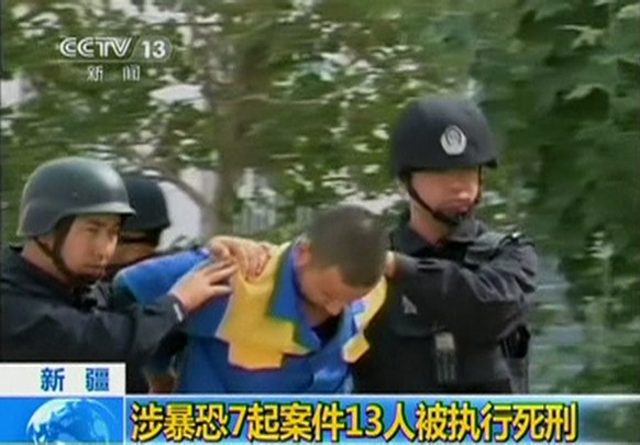 A man who is about to be executed is escorted by riot policemen in this still image taken from video in an unknown location in the Xinjiang Uighur Autonomous Region, June 16, 2014. China executed 13 p ...