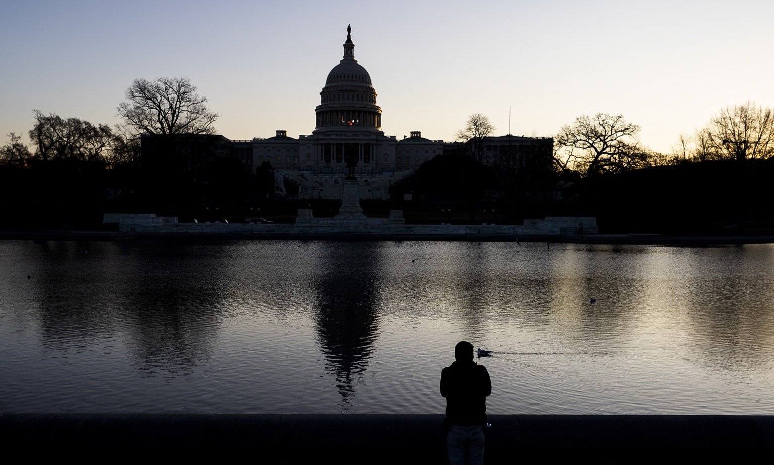 epa08924633 A man looks at the US Capitol at sunrise in Washington, DC, USA, 07 January 2021. Members of Congress certified the 2020 Electoral College early this morning following more than six hours  ...