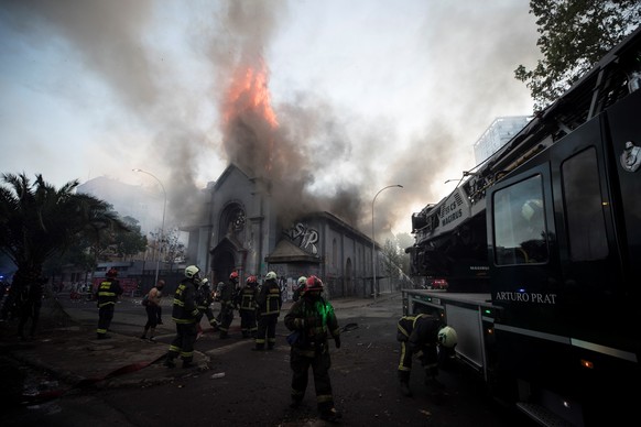 epa08756546 Firefighters work to extinguish a at the parish of La Asuncion in the surroundings of Plaza Italia,, in the aftermath of a protest in Santiago, Chile, 18 October 2020. Thousands of people  ...