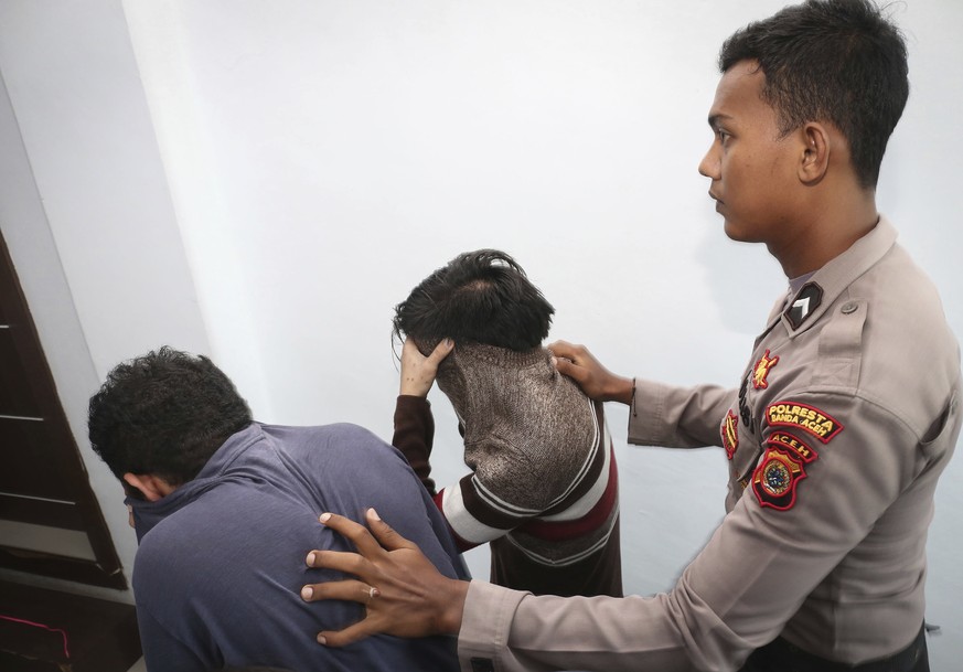 Police officer escorts two men accused of having gay sex into a holding cell to wait for the start of their trial at Shariah court in Banda Aceh, Indonesia, Wednesday, May 17,2017. A Shariah court in  ...