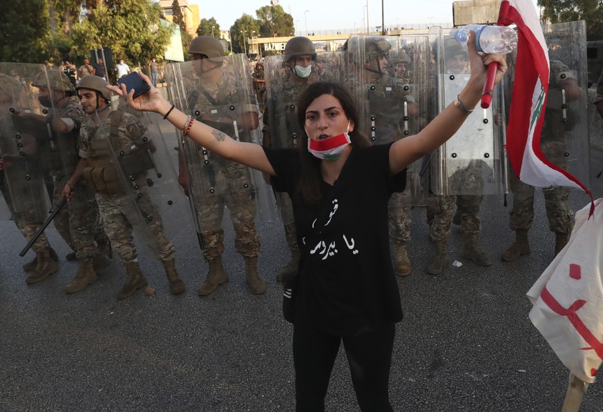 An anti-government protester tries to calm down other protesters, as she stands in front of Lebanese soldiers who bloc a road that links to the presidential palace, during a protest against the Lebane ...