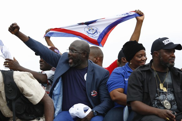 epa06237624 Liberian presidential candidate George Weah (C) from the Congress for Democratic Change (CDC) waves to supporters from a vehicle with running mate Jewel Haward-Taylor (C-R), former wife of ...