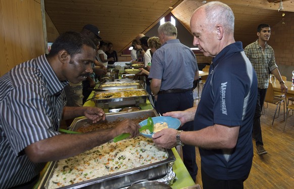 Bundesrat Ueli Maurer, rechts, laesst sich von einem Asylsuchenden Essen schoepfen bei der zweitaegigen Bundesratsreise, am Donnerstag, 2. Juli 2015, in der Asylunterkunft in Riggisberg. (KEYSTONE/POO ...