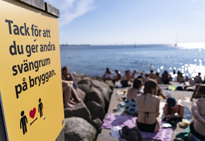 epa08509387 An information sign ask people to keep social distance due to the Covid-19 coronavirus pandemic, where people sunbathe and swim at a bathing jetty in Malmo, Sweden, 25 June 2020, during a  ...