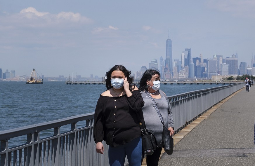 epaselect epa08384534 People in masks walk along New York Harbor in New York, New York, USA, on 25 April 2020. Restrictions requiring the shut down of all non-essential businesses are currently in pla ...