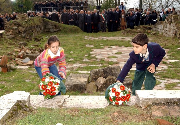 A photo of a young girl and a young boy, one from Italy and one from Germany, laying flowers on the remains of the steps of the altar of the church of San Martino - where Nazi troops burst in and shot ...