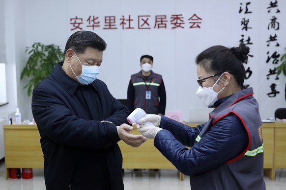 In this photo released by Xinhua News Agency, Chinese President Xi Jinping, left, wearing a protective face mask, receives a temperature check as he visits a community health center in Beijing, Monday ...